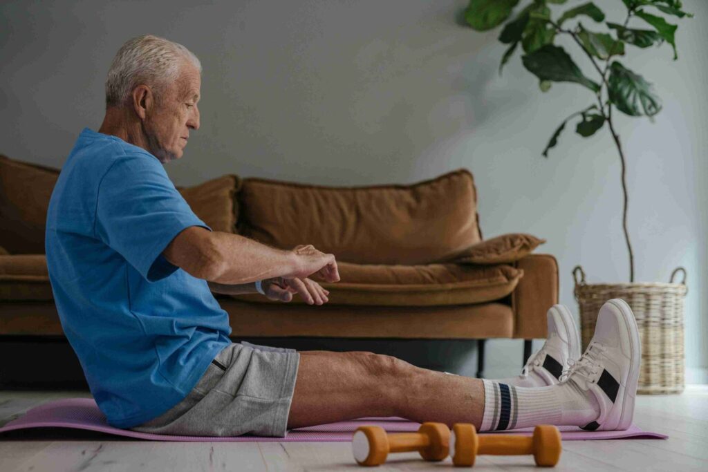 An Elderly Man in Blue Shirt and Gray Shorts Sitting on a Yoga Mat
